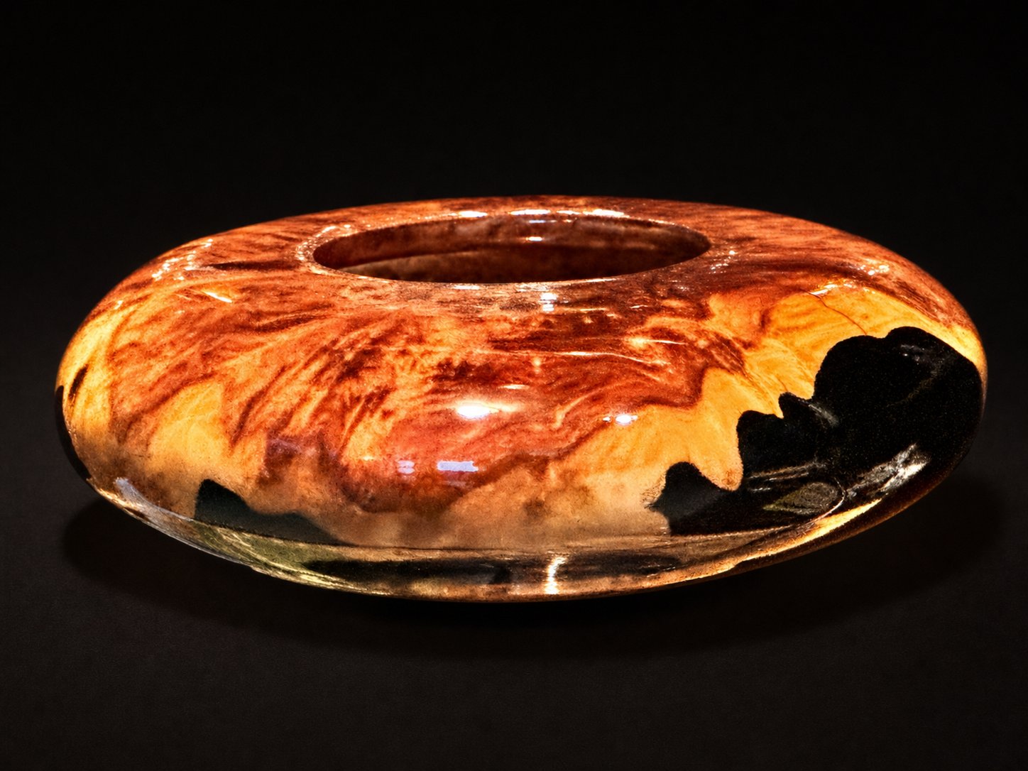 Red-orange burl ring vessel with a natural bark void, on studio black.