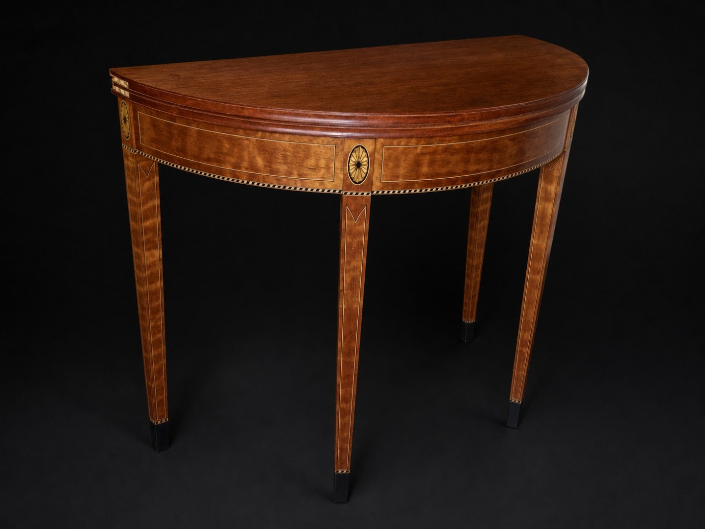A Federal-style satinwood demilune card table with brass inlay, holding a lead crystal bowl, on a studio-black background.