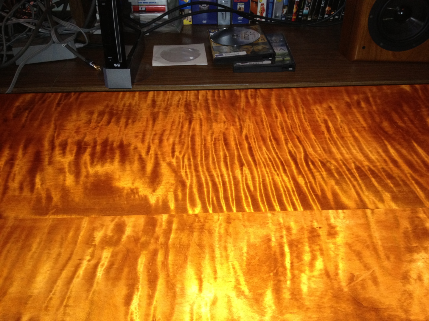 Curly maple boards under warm raking light, glowing amber with three-dimensional ripple figure.