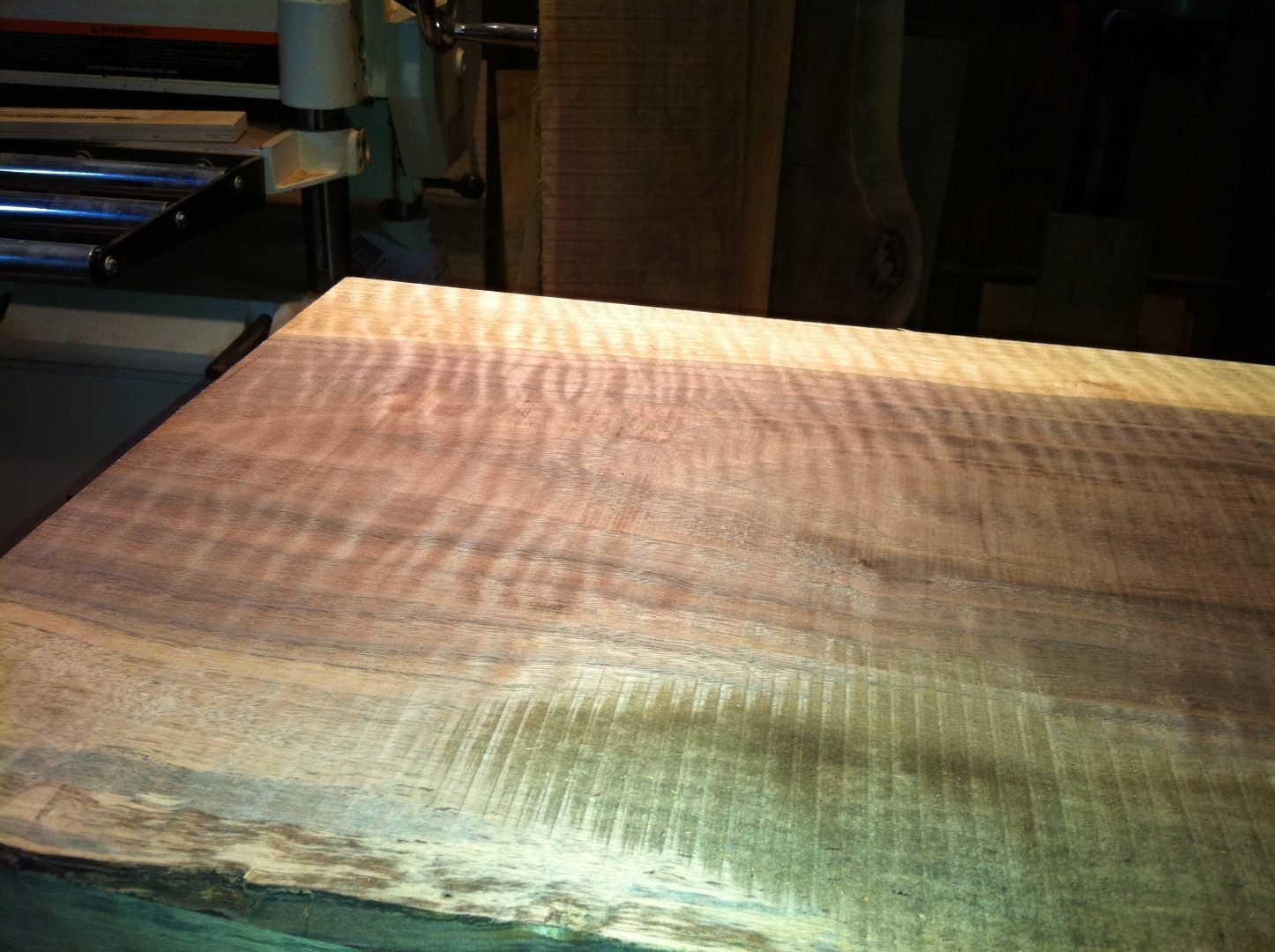 Figured walnut board on the planer, half-planed to reveal curly figure.